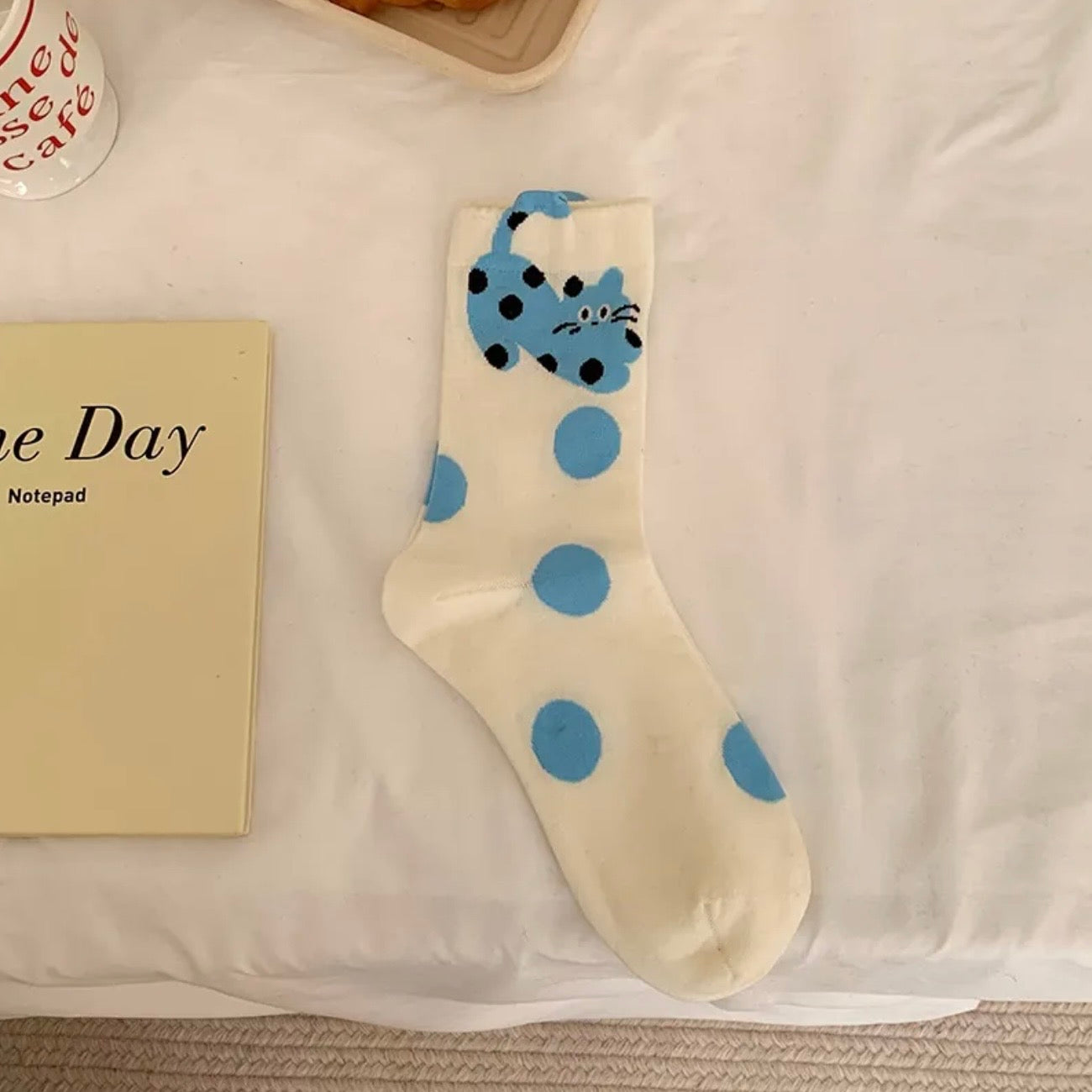 White sock with blue polka dots and a cat design on a white surface.