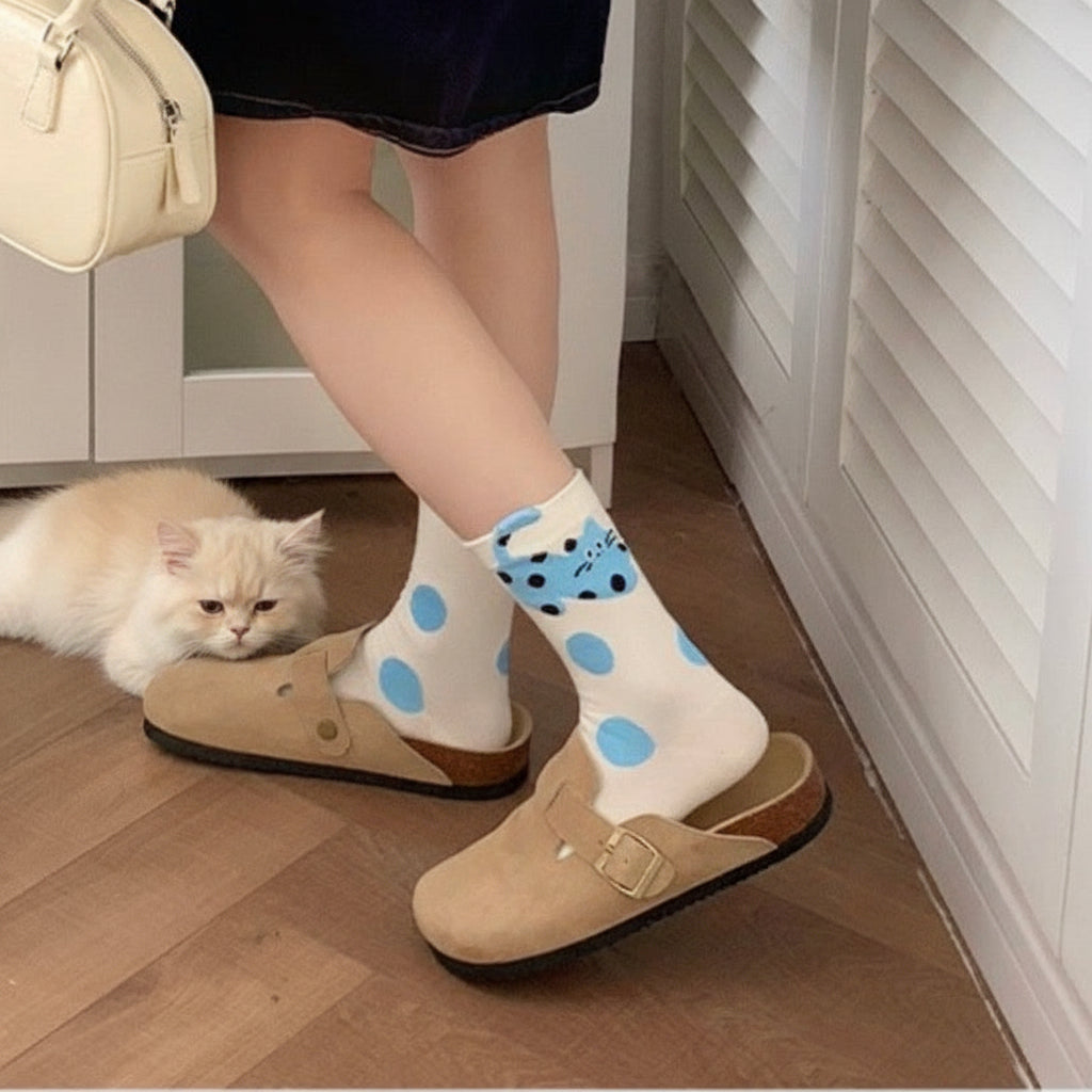 Person wearing white socks with blue polka dots and beige shoes on a wooden floor.