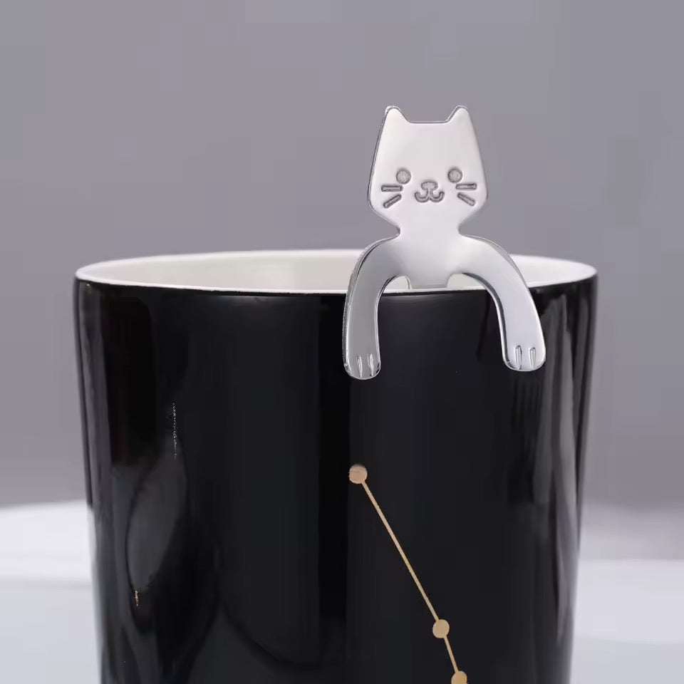 Cat-shaped spoon on a black mug against a gray background