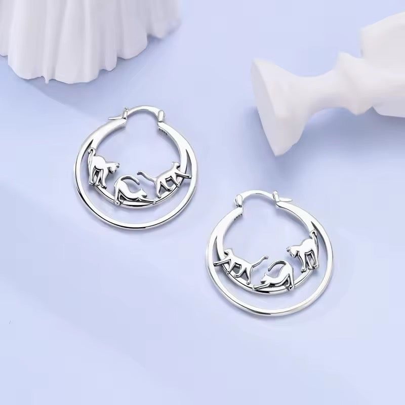 Silver hoop earrings with acrobatic cats in unique poses on a light purple background