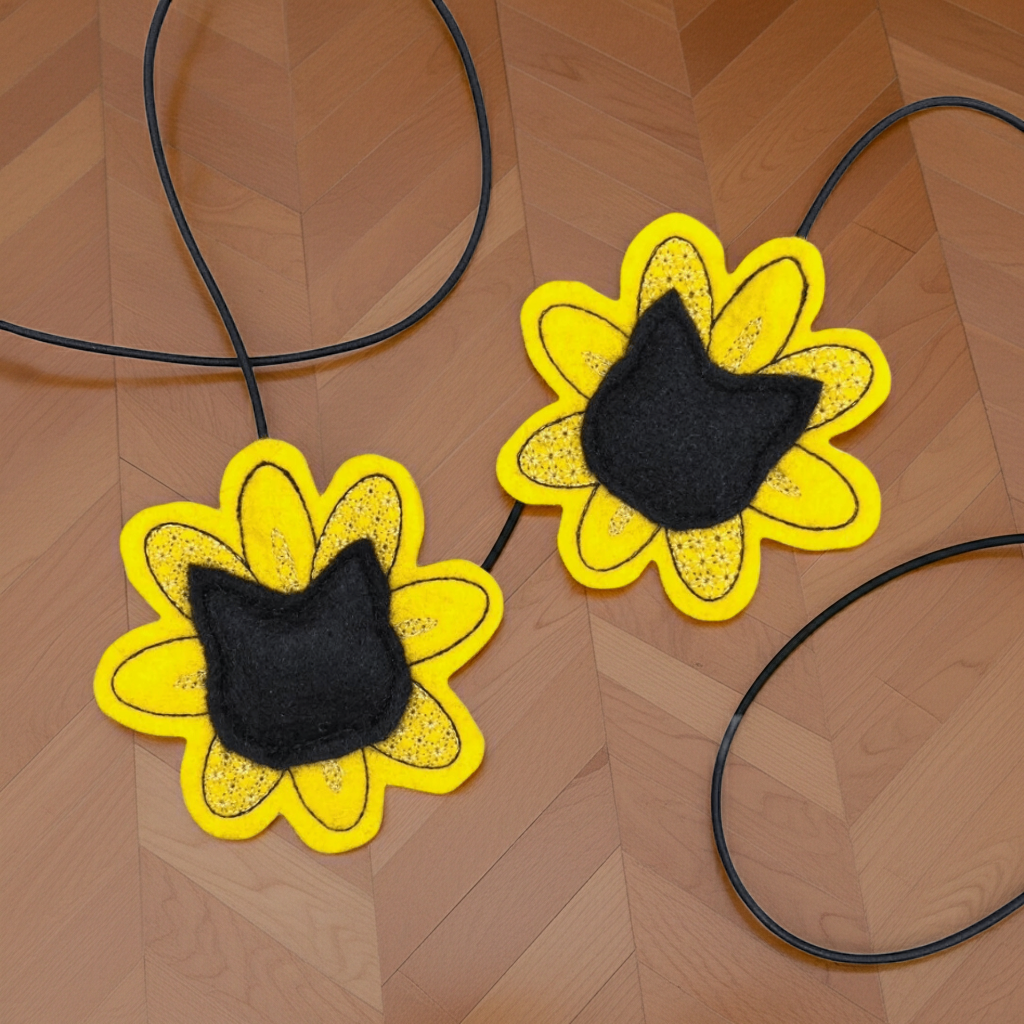 Two yellow flower-shaped cat toys with black cat head shaped centers on a wooden surface