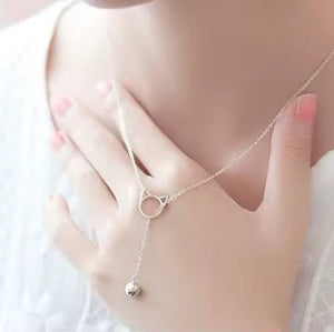 Silver necklace with a small pendant worn by a person against a white background