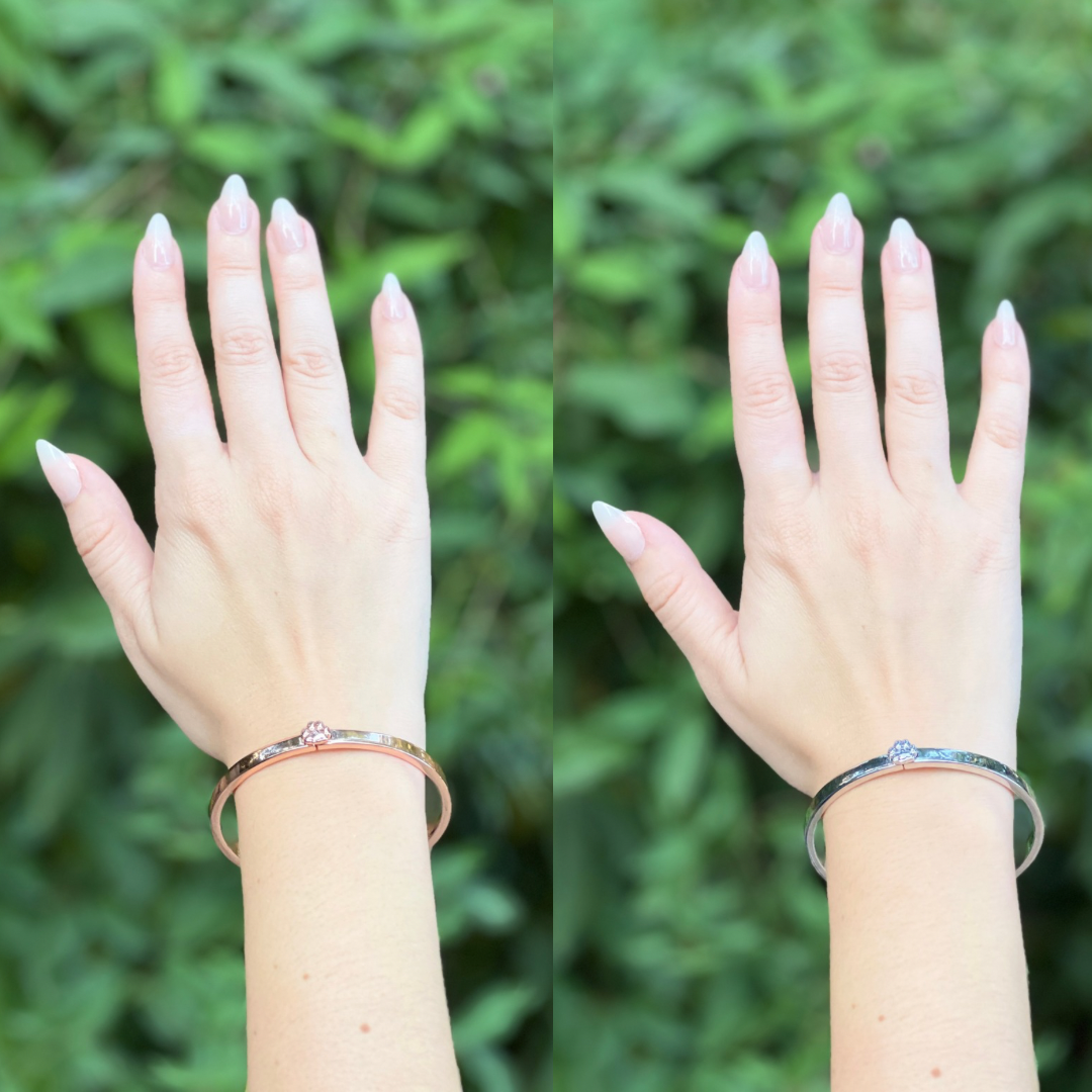 Hands wearing a gold bangle bracelet with a gold paw print next to a hand wearing a silver bangle with a silver paw print