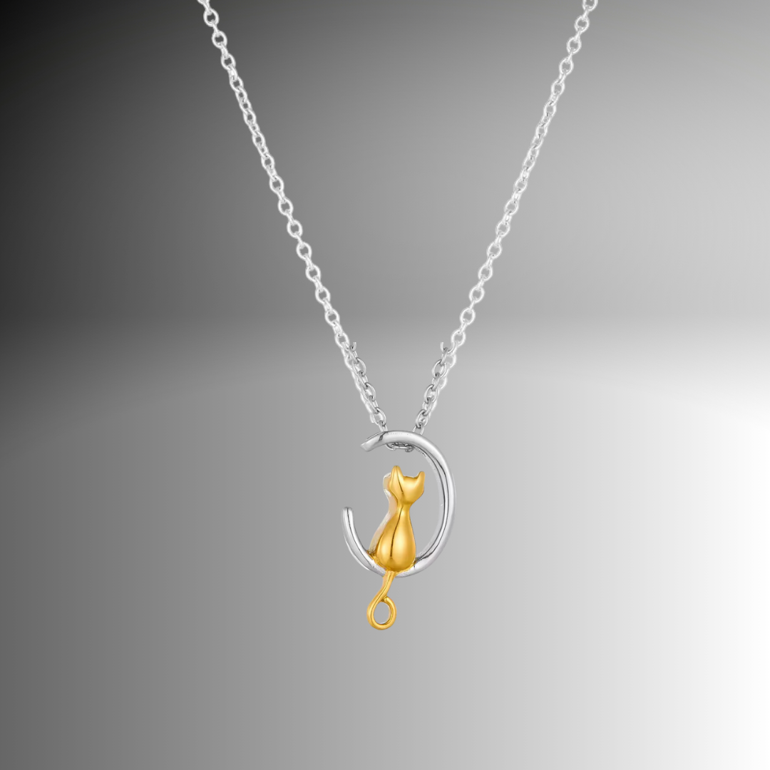 A pendant with a silver cat sitting on a crescent moon dangles from a silver necklace. The pendant is a keepsake memorial that holds favorite pet’s ashes.