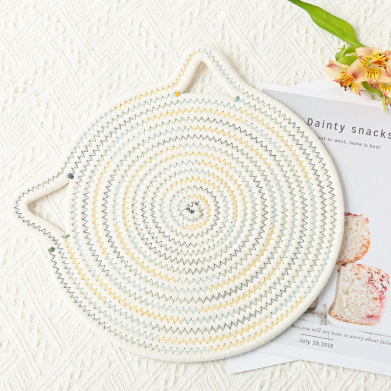 Multi color seven inch hot pad trivet shaped like a cat head on a magazine on a table