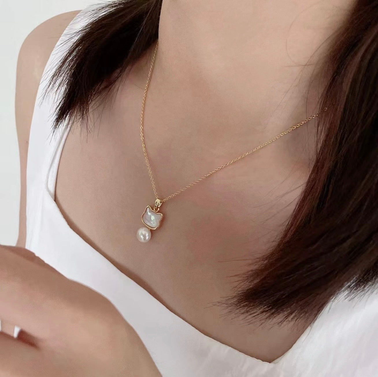 Necklace with a cat-shaped pendant and pearl on a person wearing a white top.