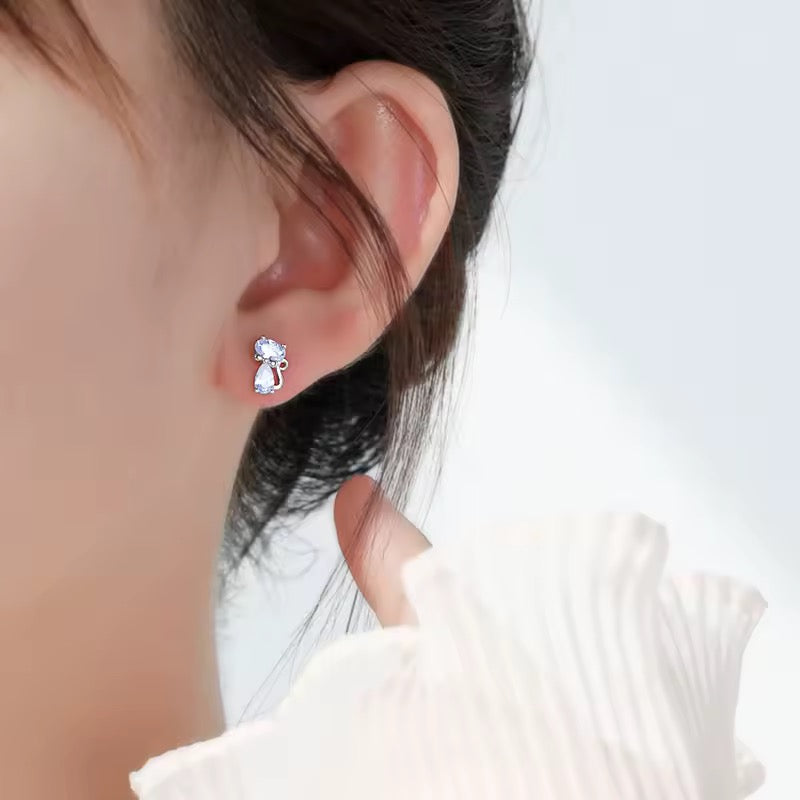 Close-up of an ear wearing a sparkly clear crystal cat with curly tail on a woman with dark hair.