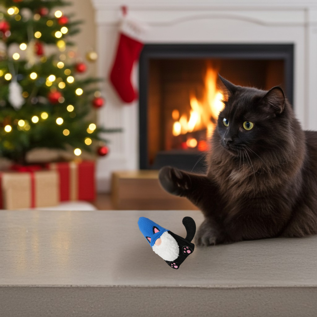 Black cat sitting on a couch with a Christmas gnome toy in front of a fireplace and decorated Christmas tree.