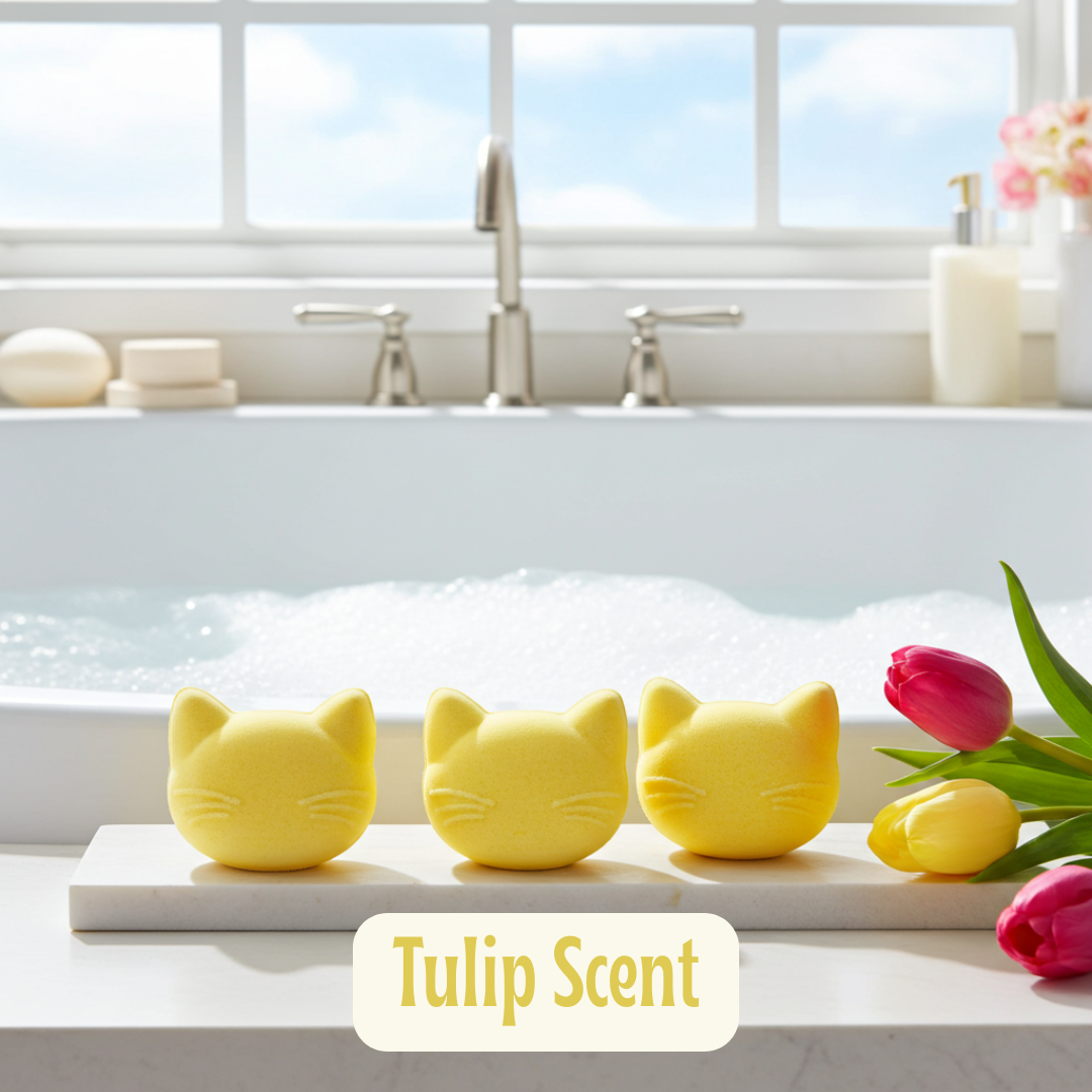 Three yellow cat-shaped bath fizzies on a marble slab with tulips and a bathtub in the background.