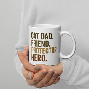 person holding white mug that says cat dad, friend, protector, hero