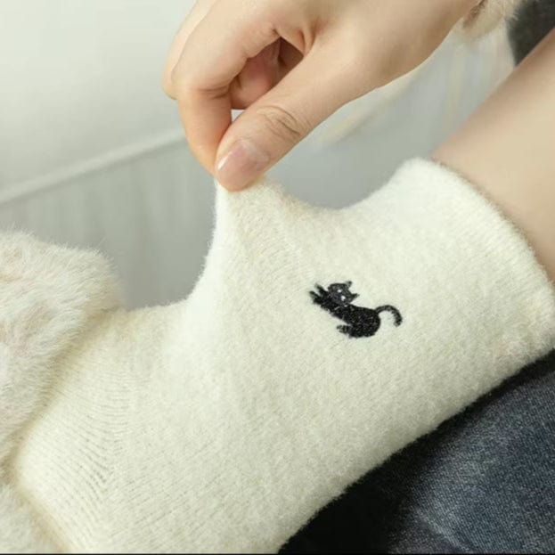 Person wearing white fuzzy sock with embroidered black cat on the upper part of the sock