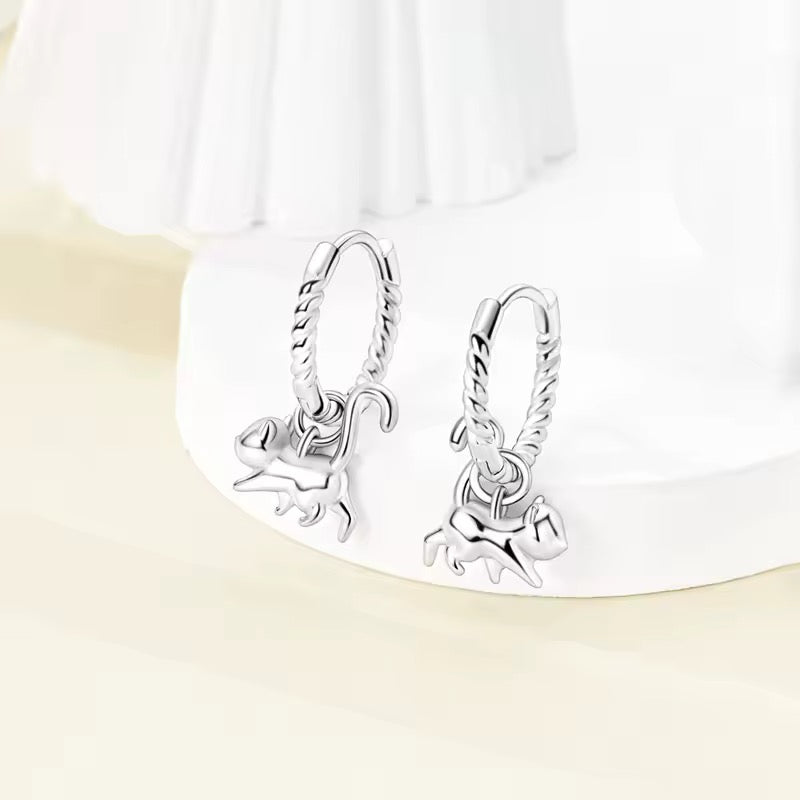 Silver earrings with dangling cat charms on a white background