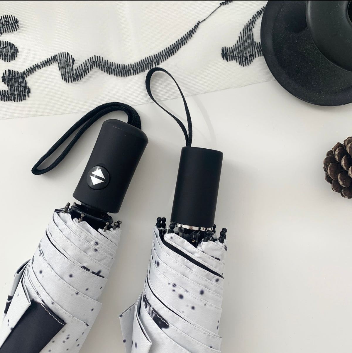 Two folded umbrellas with black handles and a black cat design on a white surface.