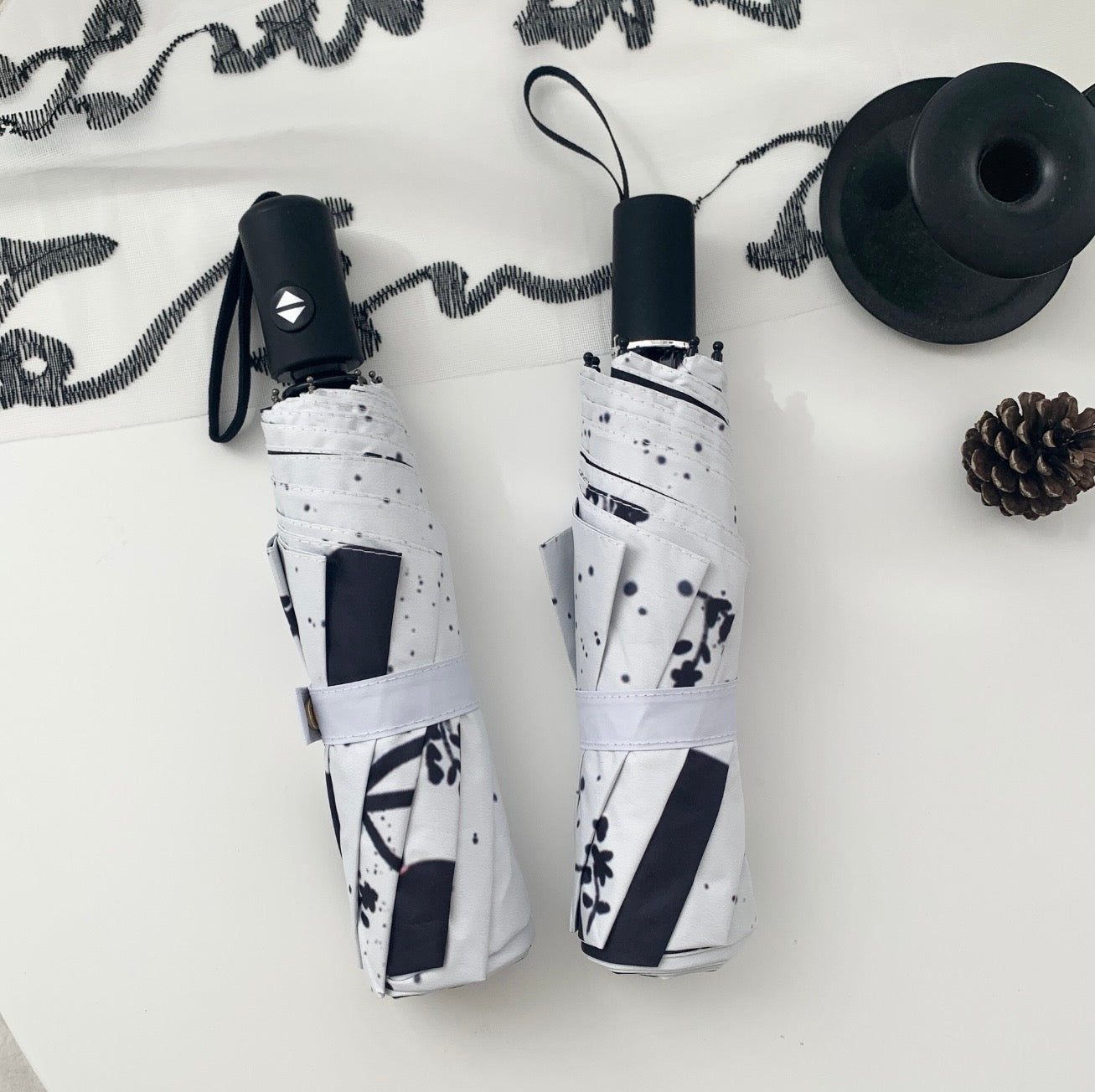 Two folded umbrellas with Black Cat design on a light surface.