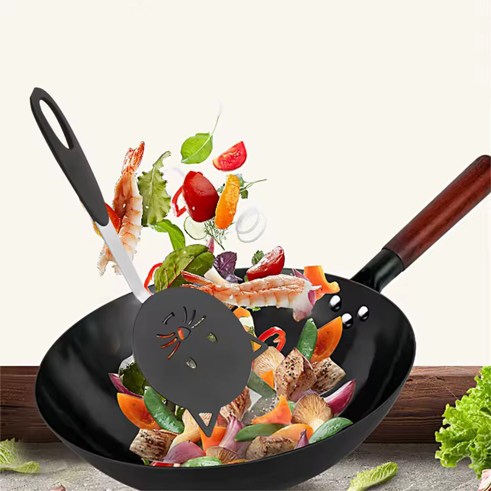 Black wok with colorful vegetables being tossed by a Triple T Studios Black Cat Spatula on a white background