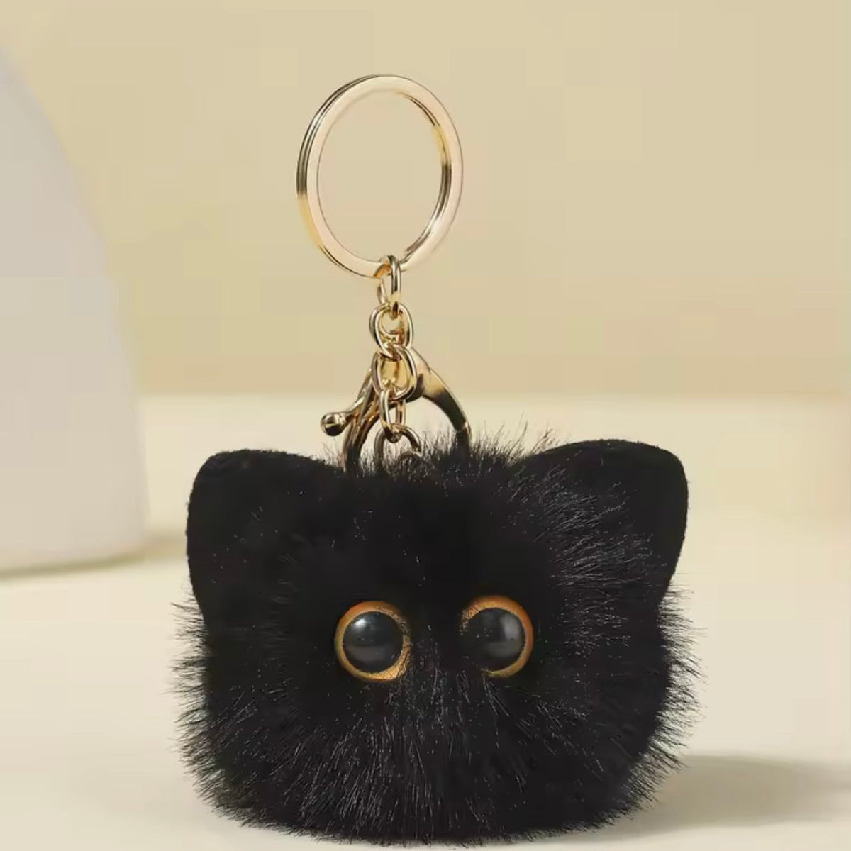 Black cat-shaped keychain with gold accents on a beige background