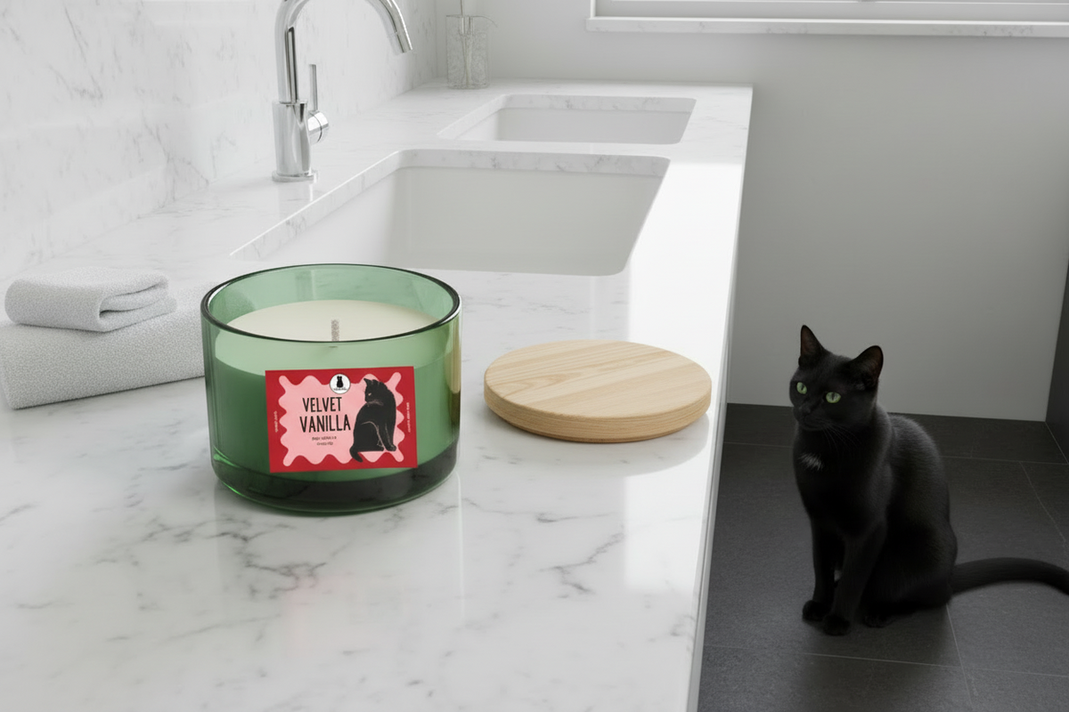 Vanilla Velvet glass candle with a bamboo lid sitting on a bathroom counter. Black cat sitting on floor nearby.