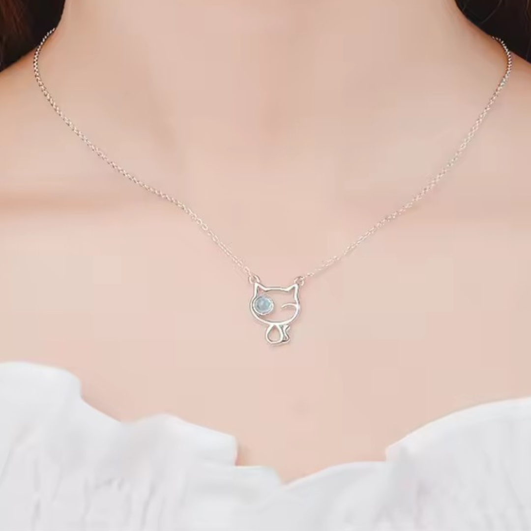 Cat-shaped necklace with a small round pendant on a person wearing a white top.