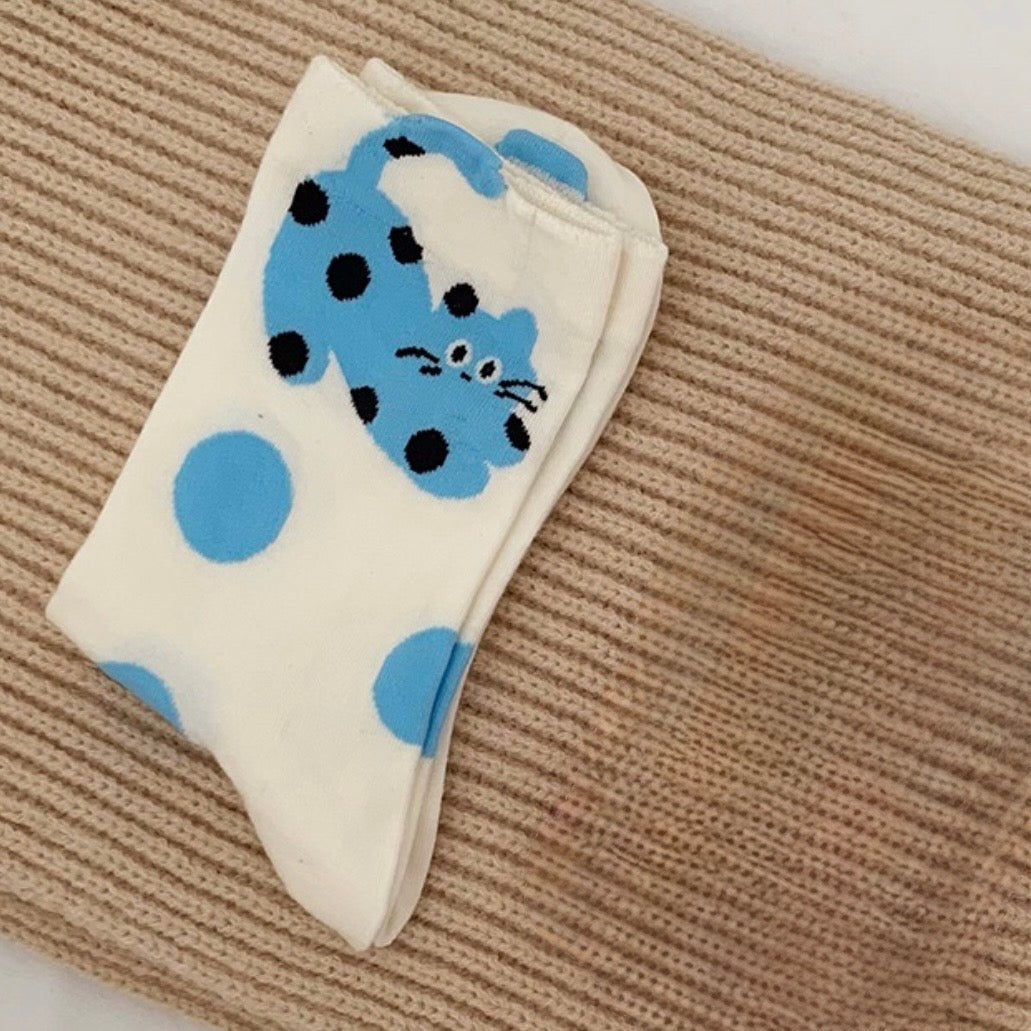 Pair of socks with blue polka dots and cat design on a beige surface