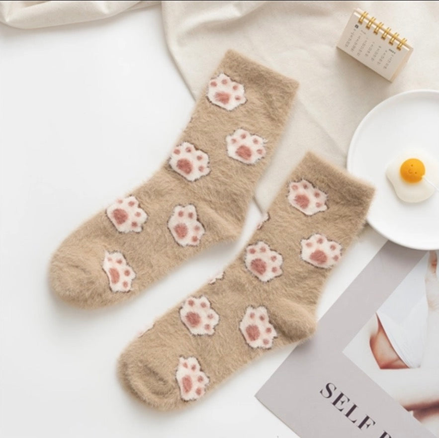 Beige fuzzy warm winter socks with cat paw prints on a white surface with a magazine and small notebook.