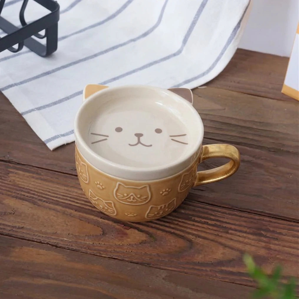 A ceramic cat-themed mug with a handle shaped like a cat ear, featuring a cream-colored top with a printed cat face and a brown lower body decorated with cat illustrations, shown on a wooden tabletop.