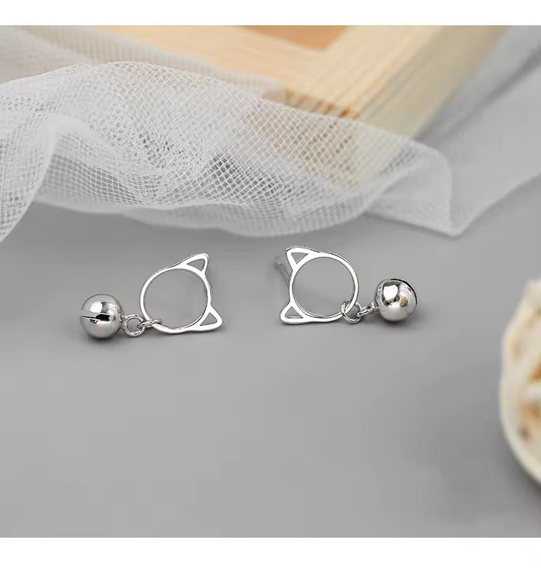 Silver cat ear-shaped earrings on a gray surface with a white fabric background