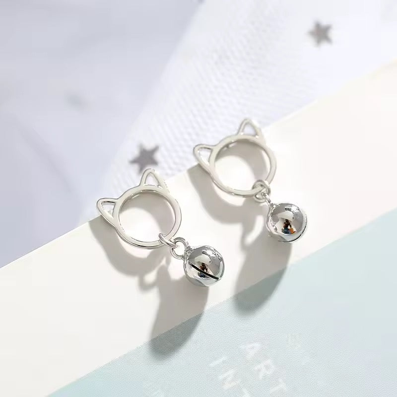 Silver cat ear-shaped earrings with small bells on a light background