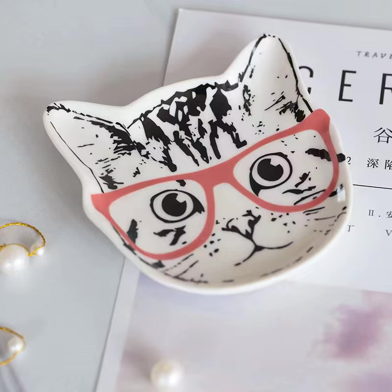 Cat-shaped dish with a face design wearing pink glasses on a white surface.