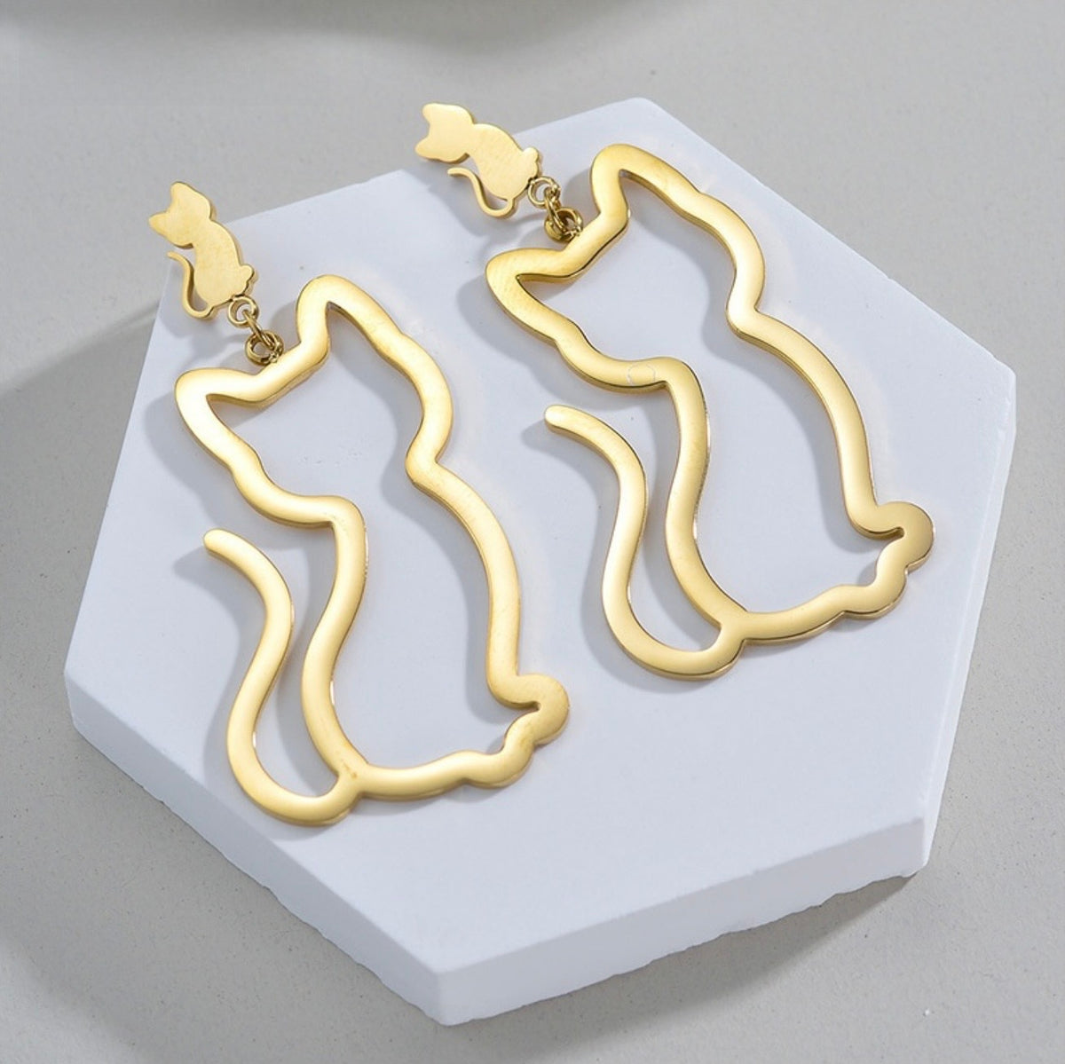 Gold abstract earrings on a white hexagonal stand against a gray background