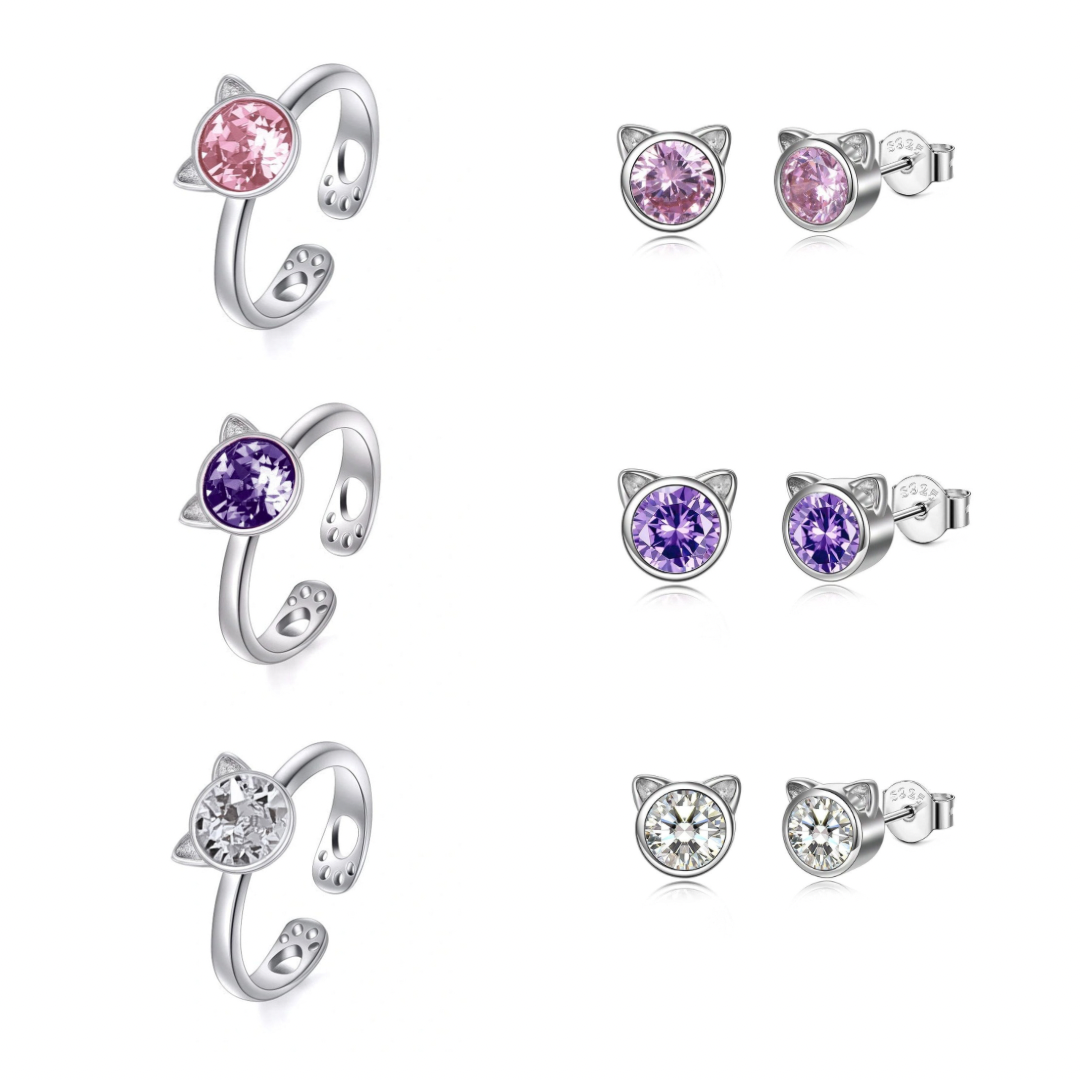 Three sets of cat-shaped earrings and rings with colorful shiny crystals on a white background