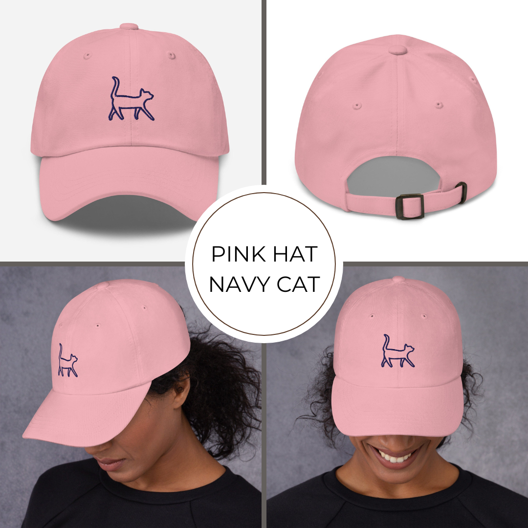 Pink hat with navy cat logo worn by a person on a gray background