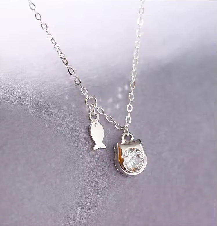 Silver necklace with a fish charm and round pendant on a light gray background