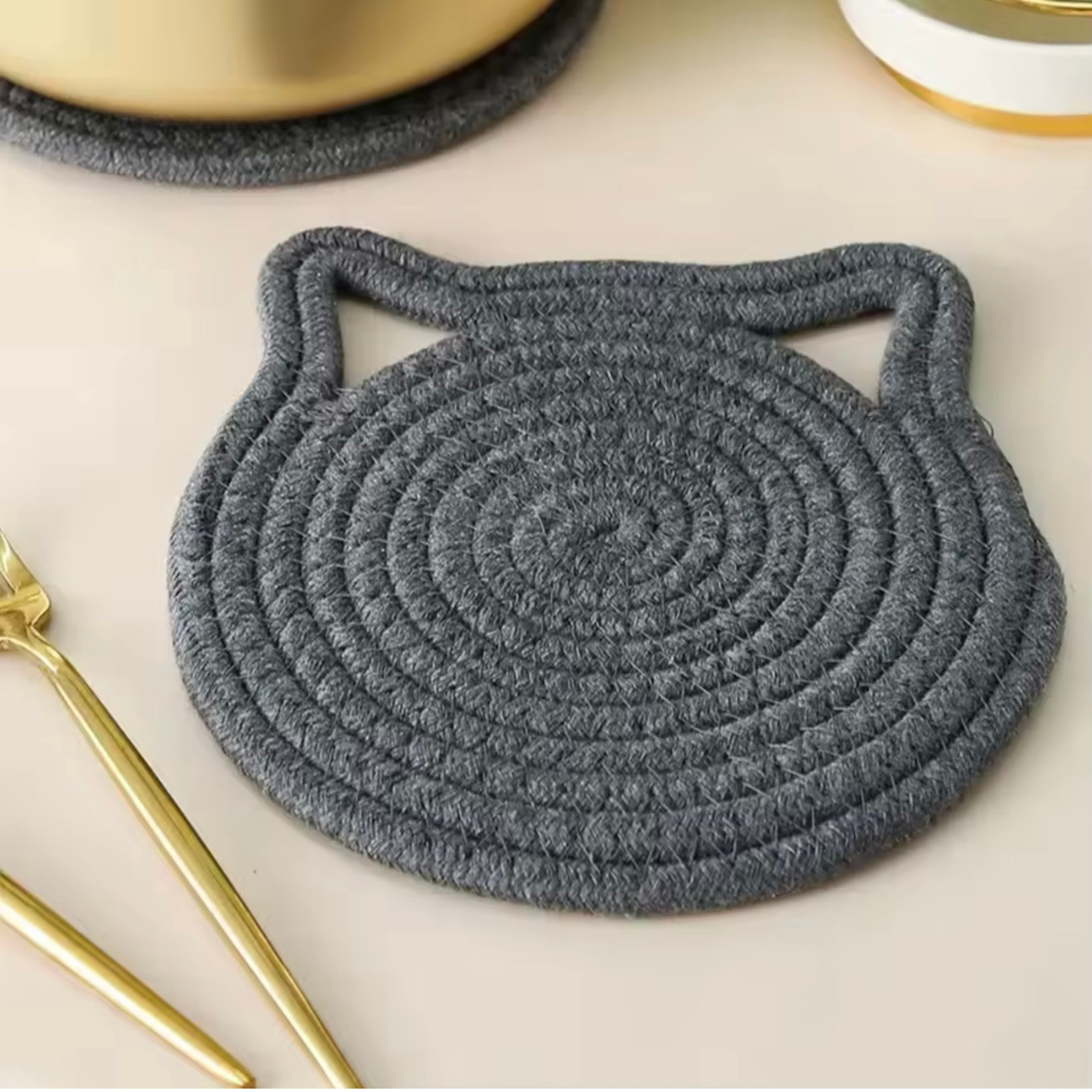 Gray woven Cat Ear trivet on a light surface with gold accents