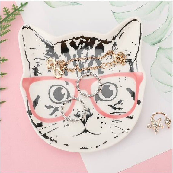 Cat-shaped jewelry dish with rings on a pink and white background