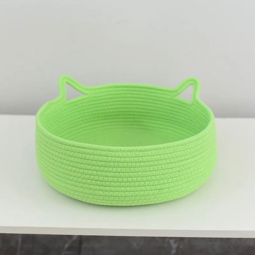 A bright lime green woven rope basket with Cat Ears, shown on a white shelf against a light gray wall.