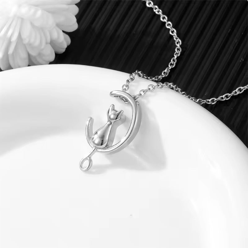 Silver necklace with a silver Cat on a Crescent Moon pendant that holds ashes to wear as a keepsake for a lost pet. Necklace drapes across a white dish.