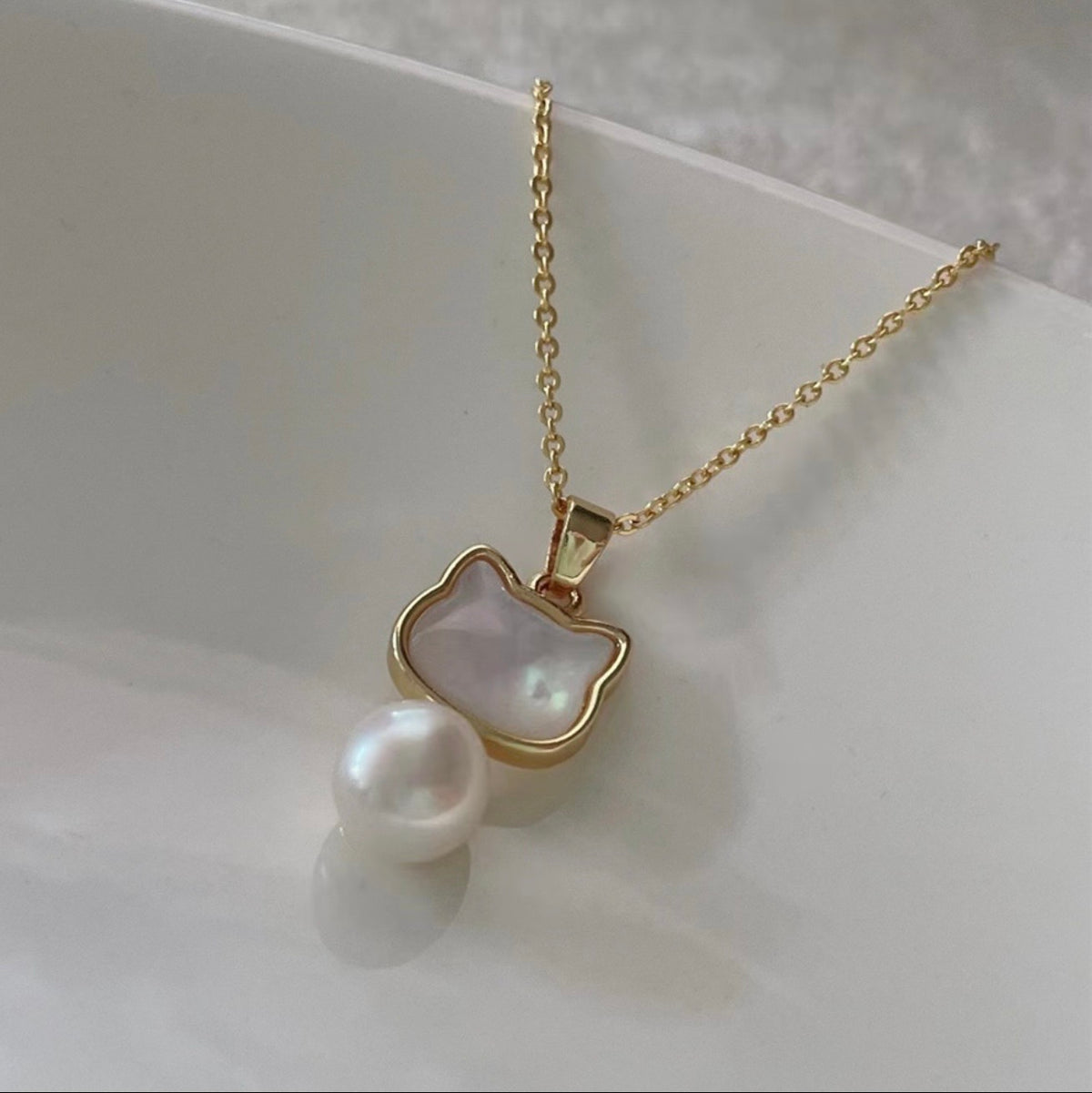 Gold necklace with a cat-shaped mother of pearl pendant and pearl on a white background