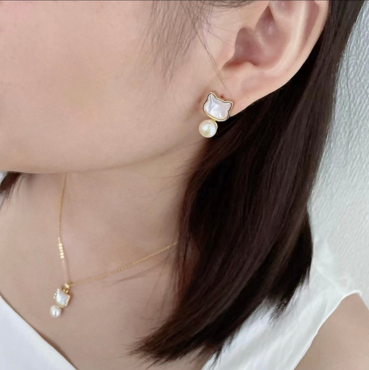Cat-shaped earring and necklace with pearl detail worn by a person