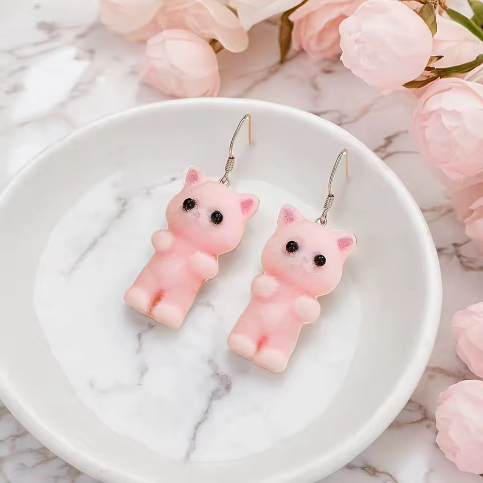 Pink cat-shaped earrings on a white dish with pink flowers in the background