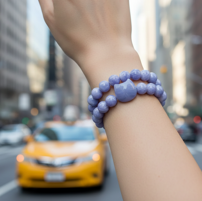 Woman’s wrist shown wearing a purple beaded bracelet with a Cat Head accent bead with a city street in the background