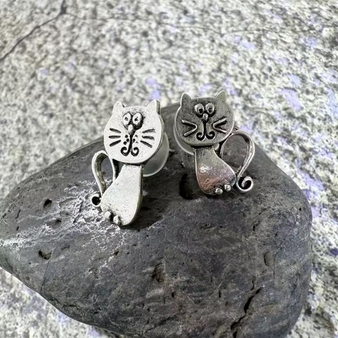 Silver cat-shaped earrings on a dark stone surface