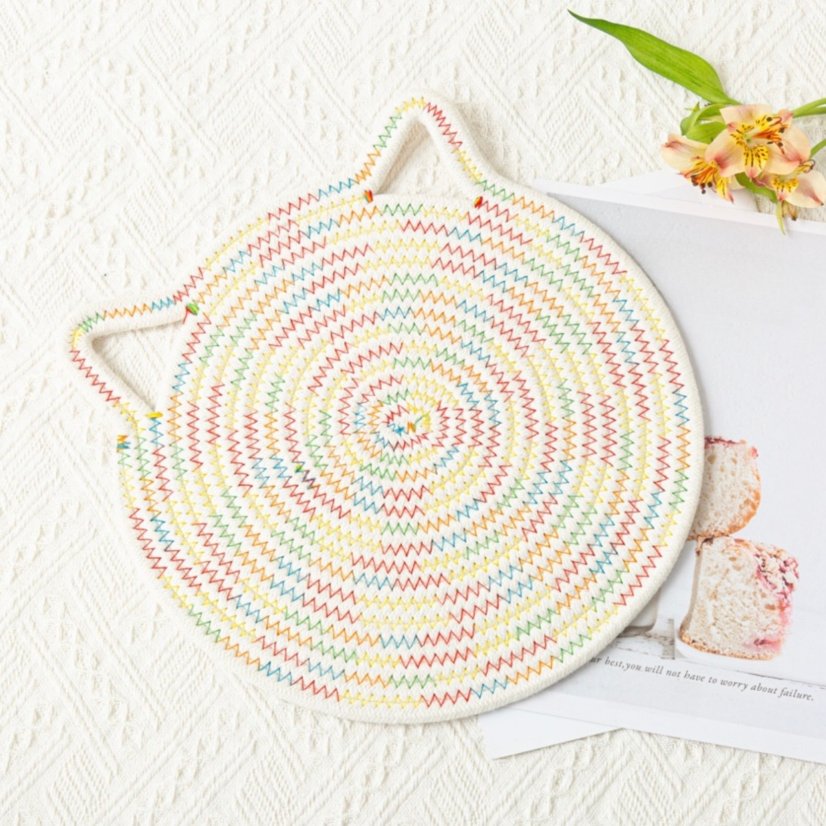 Round, multicolored woven trivet hot pad on a table with a magazine underneath.