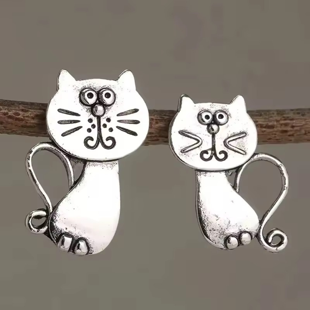 Silver cat-shaped earrings on a wooden stick against a gray background
