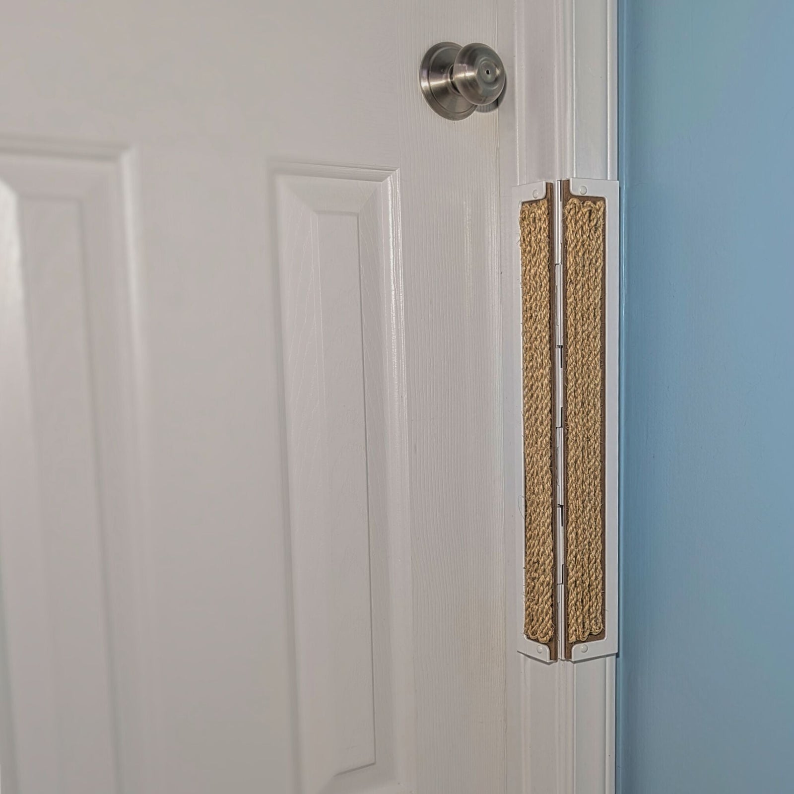A Sisal Cat Scratcher attached to the right side of a white paneled door, next to a light blue wall.