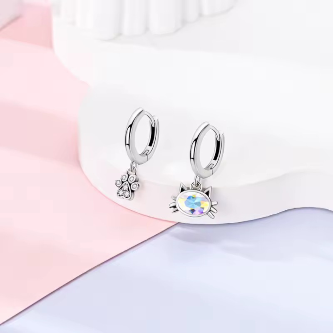 Silver hoop earrings with cat paw and cat head charms on a pastel background