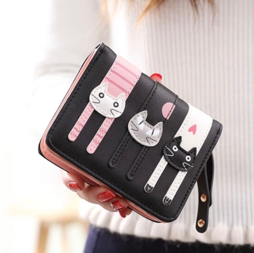 Black wallet with cat designs held by a person wearing a white sweater.