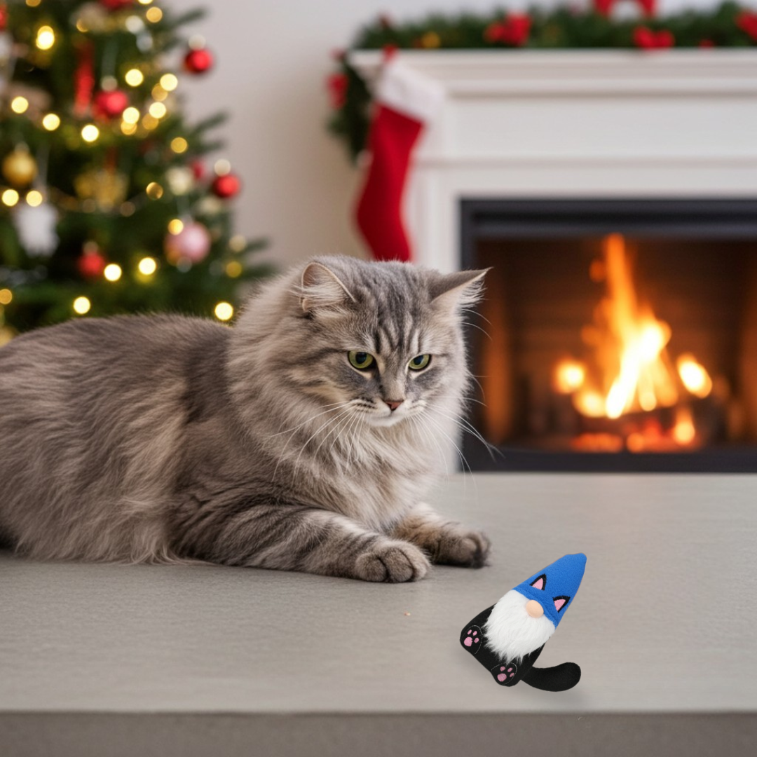 Cat lying on a surface playing with a Black Cat Gnome with a Christmas tree and fireplace in the background