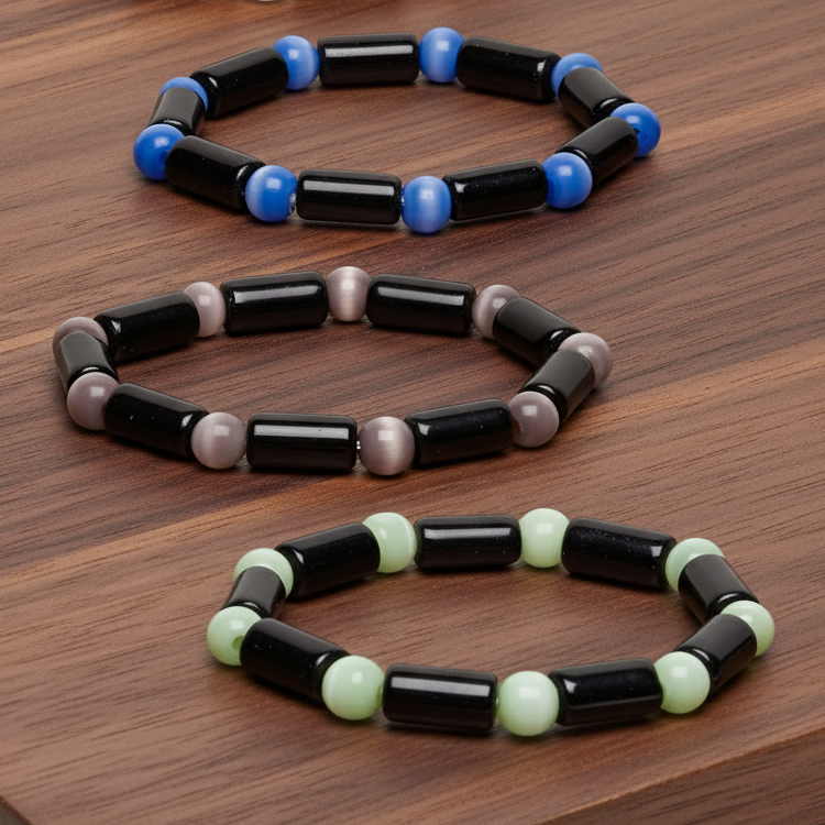 Three beaded glass Cat Eye bracelets in black, blue, and green on a wooden surface