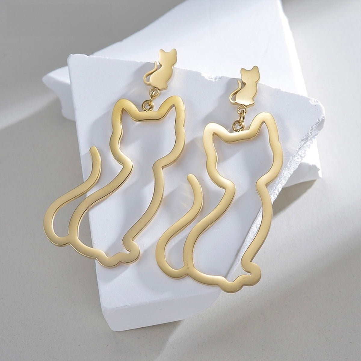 Gold cat-shaped earrings on a white pillow