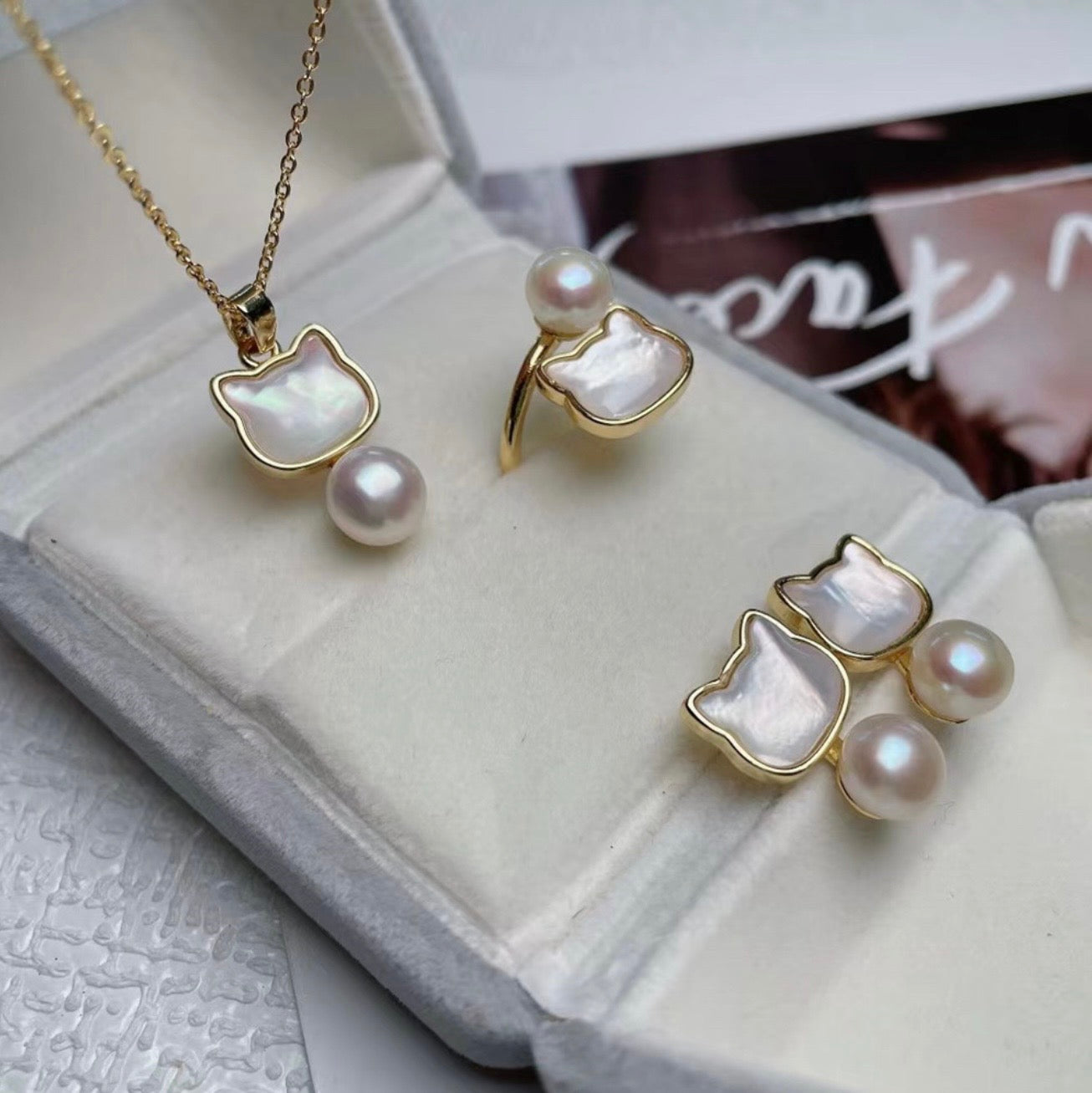 Pearl jewelry set with gold cat-shaped pendants on a textured surface